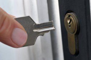 Close-up of a hand holding a key partially inserted into a door lock.