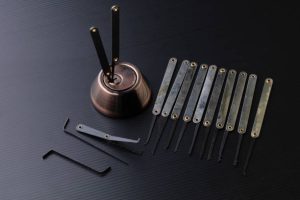 A set of lockpicking tools, including tension wrenches, picks, and a practice lock, is arranged on a dark surface.