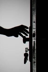 A silhouetted hand reaches for a doorknob on a partially open door with keys hanging from the lock.