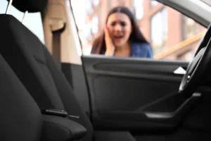 A woman stands outside a car with the door open, looking distressed; a car key is visible on the driver's seat inside.