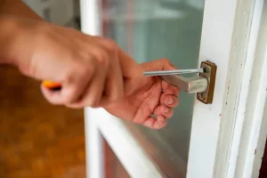 A person using a screwdriver to repair or adjust the handle of a white door. Locksmith in Cliffside Locksmith in Mount Dennis Locksmith in St. Clair West Best Locksmith for Queen Street West Apartments: Speed + Security
