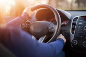 Person driving a car, holding the steering wheel with both hands. Sunlight is shining through the window, and the dashboard is visible. Automotive Locksmith in Thorncliffe Park Quick Guide: When You Should Call a Locksmith for Your Vehicle Can a Locksmith in Toronto Help With Car Lockouts?