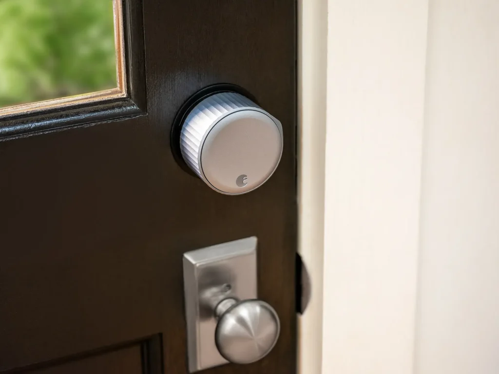 A smart door lock with a metal finish is installed above a standard door knob on a dark wooden door, reflecting what are the best smart locks for Toronto condos in terms of style and security. How Technology Is Changing Locksmith Services: Virtual Quoting, Keyless Entries, and More