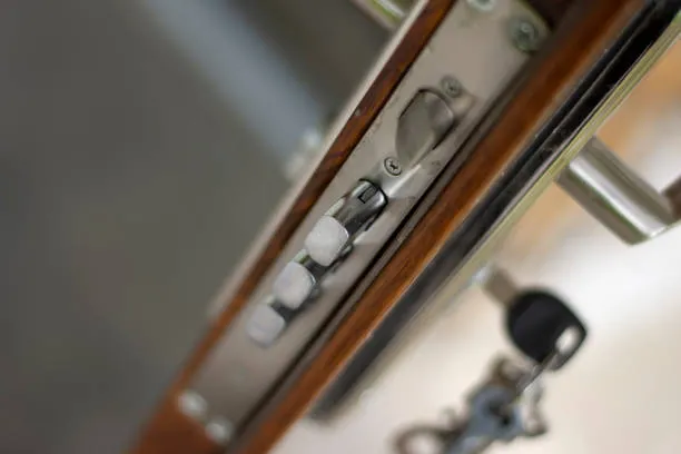 Close-up view of a metal door latch mechanism on a wooden door, with a key inserted in the lock and the handle partially visible.