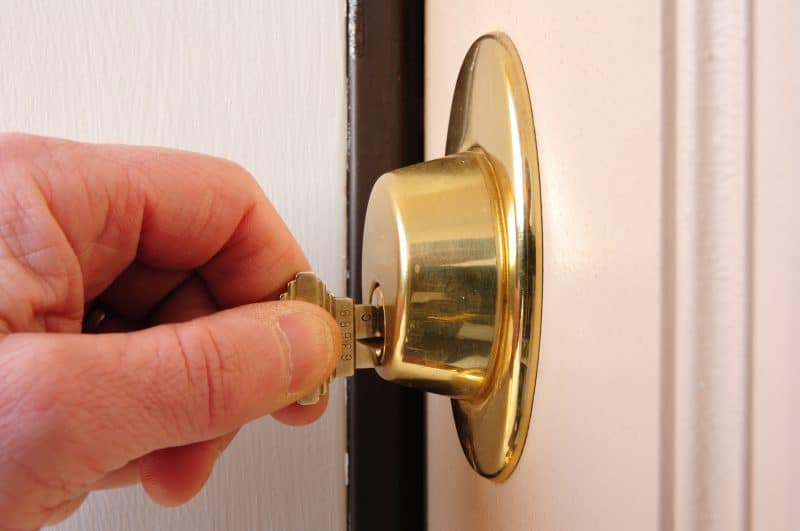 A hand inserting a key into a gold-colored deadbolt lock on a white door.