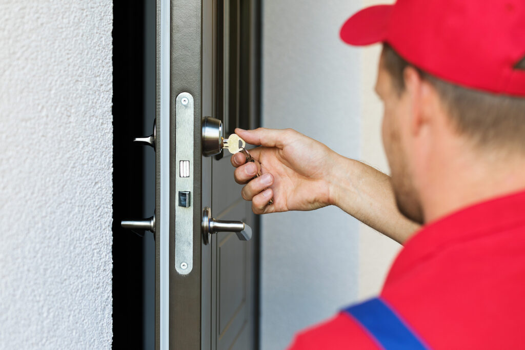 A person in a red uniform is inserting a key into the lock of a metal door.